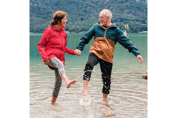 Image Elderly couple laughing and standing with their feet in the water.
